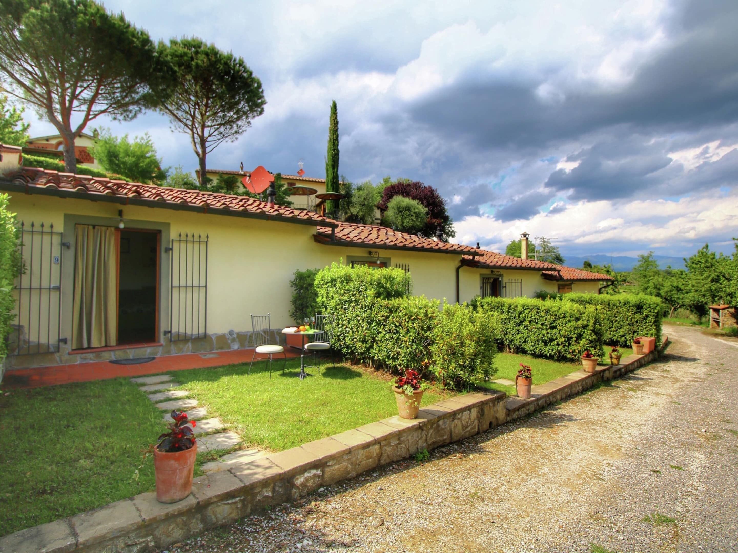 A yellow villa with a tiled roof, a stone pathway, and neatly trimmed hedges.