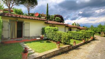 A yellow villa with a tiled roof, a stone pathway, and neatly trimmed hedges.