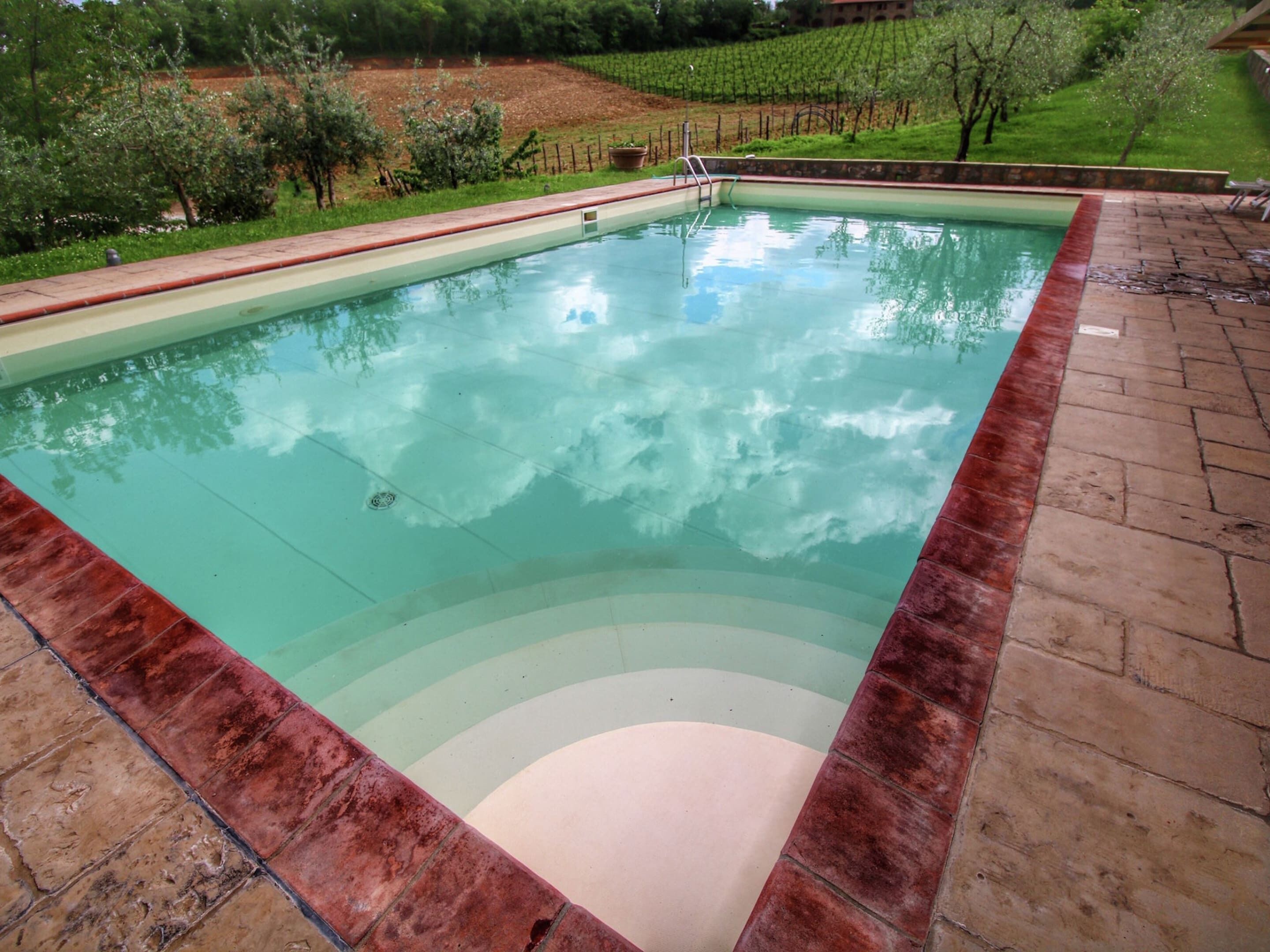 A rectangular swimming pool with a red border, surrounded by a brick patio.