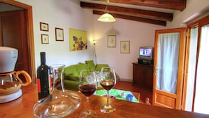 Een gezellige woonkamer met een houten plafond, een groene bank, een koffiezetapparaat, wijnglazen en een televisie op een houten kast.