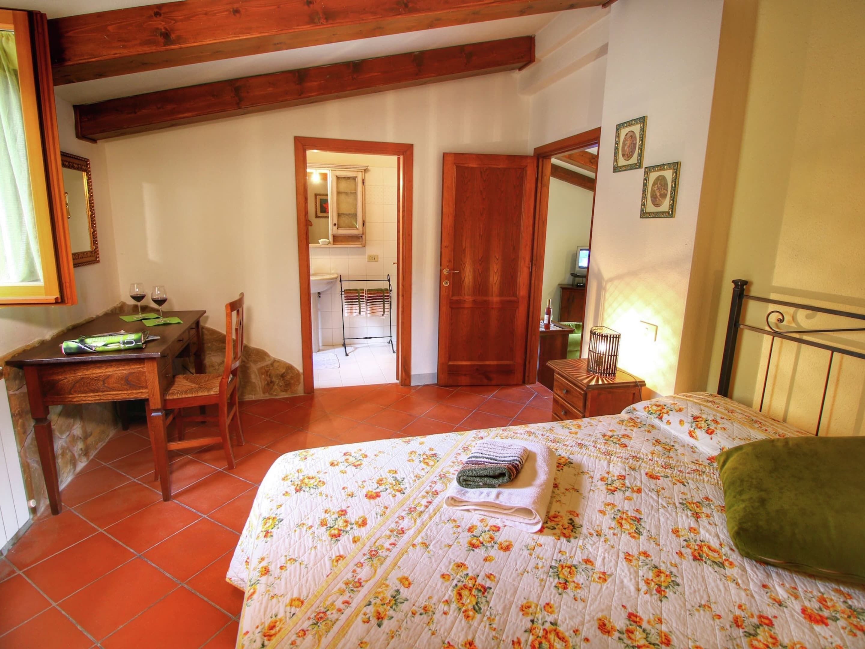 A bedroom with a bed, a desk, a chair, and a bathroom visible through an open door.