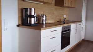 A modern kitchen with wooden cabinets, a stainless steel coffee maker, a kettle, and a dishwasher. - Lush Apartment in Furtwangen near Black Forest with Balcony (Furtwangen)