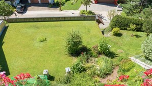 A well-maintained lawn with a variety of plants and flowers, a paved driveway, and a building in the background. - Lush Apartment in Furtwangen near Black Forest with Balcony (Furtwangen)