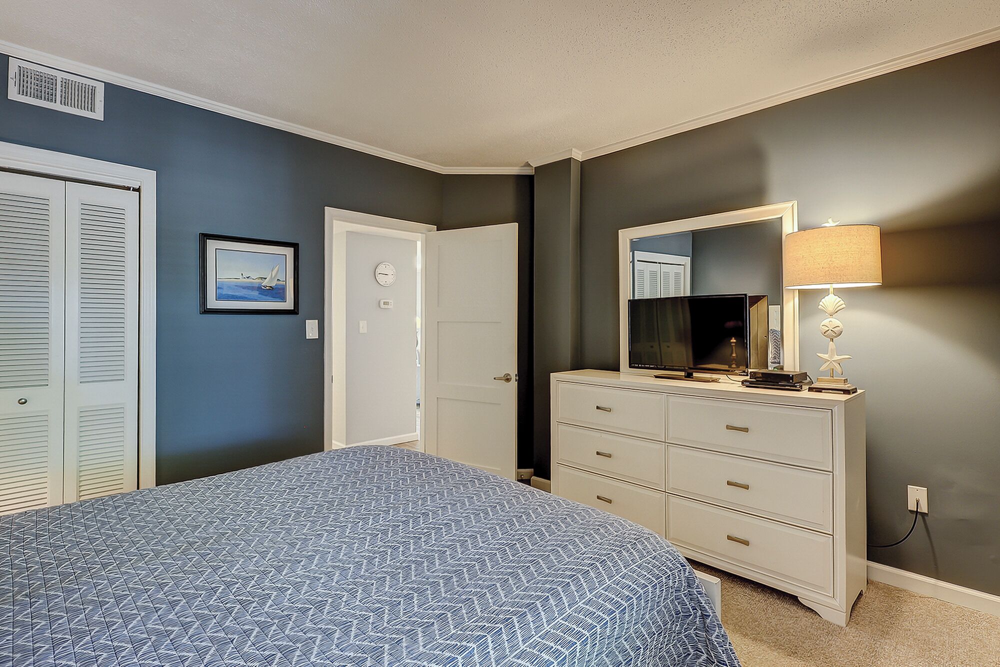 A bedroom with a bed, a dresser, a mirror, and a lamp.