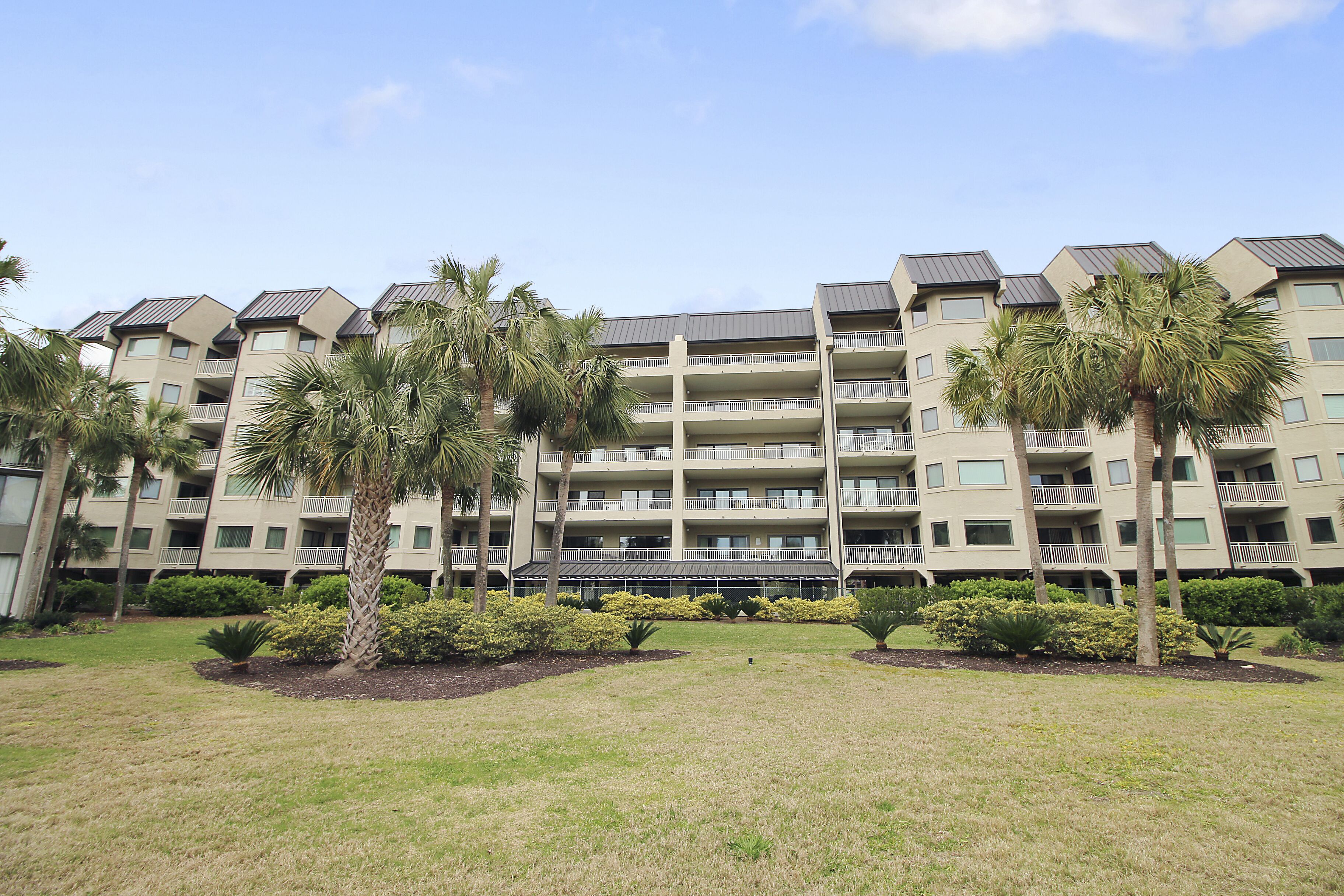 A multi-story hotel with balconies, palm trees, and a well-maintained lawn.