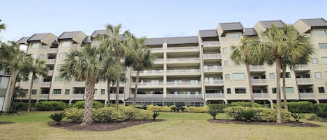 A multi-story hotel with balconies, palm trees, and a well-maintained lawn.