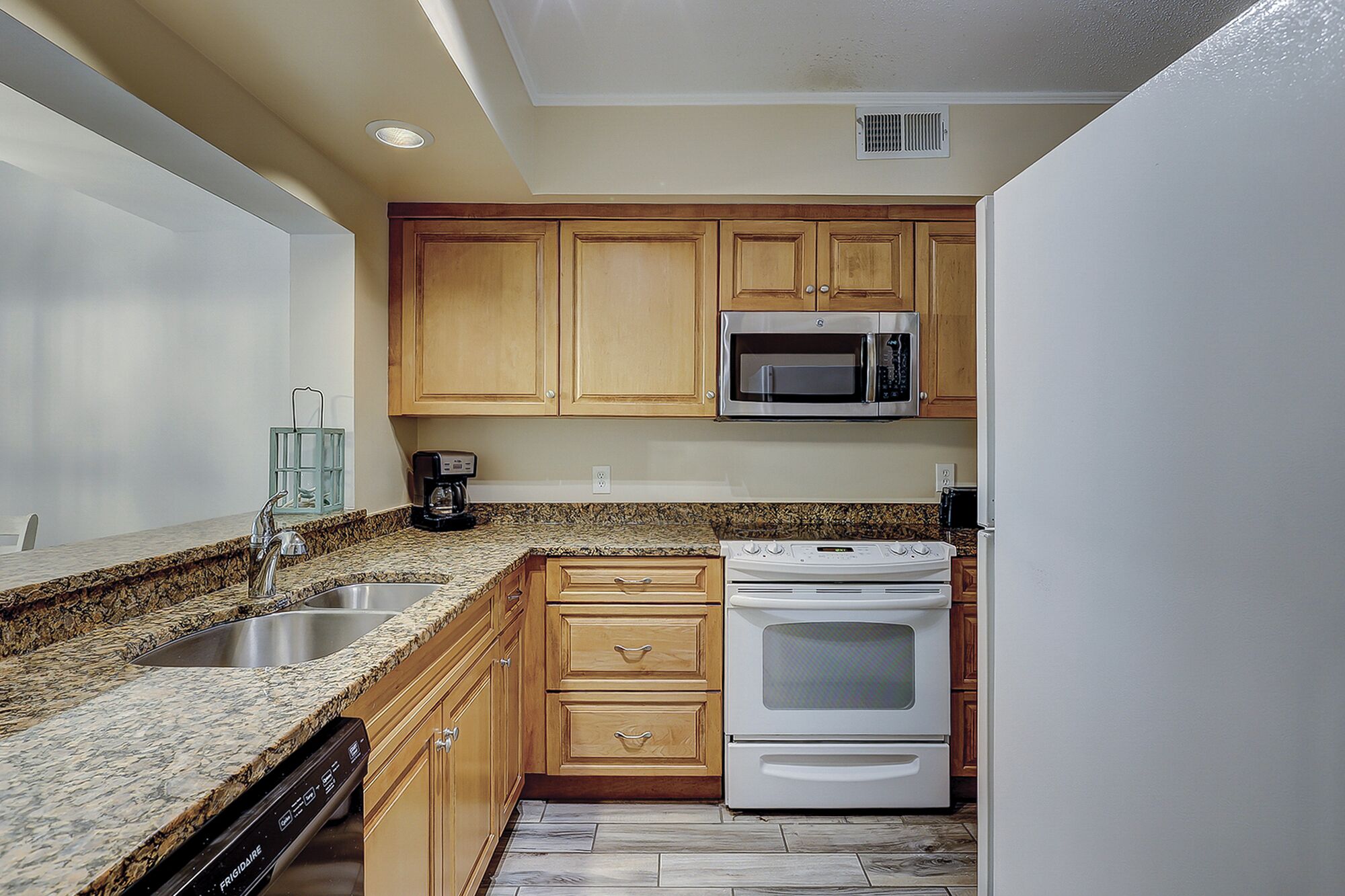 A kitchen with granite countertops, wooden cabinets, a stainless steel sink, a built-in microwave, and a white stove.