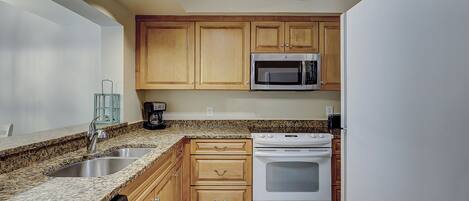 A kitchen with granite countertops, wooden cabinets, a stainless steel sink, a built-in microwave, and a white stove.