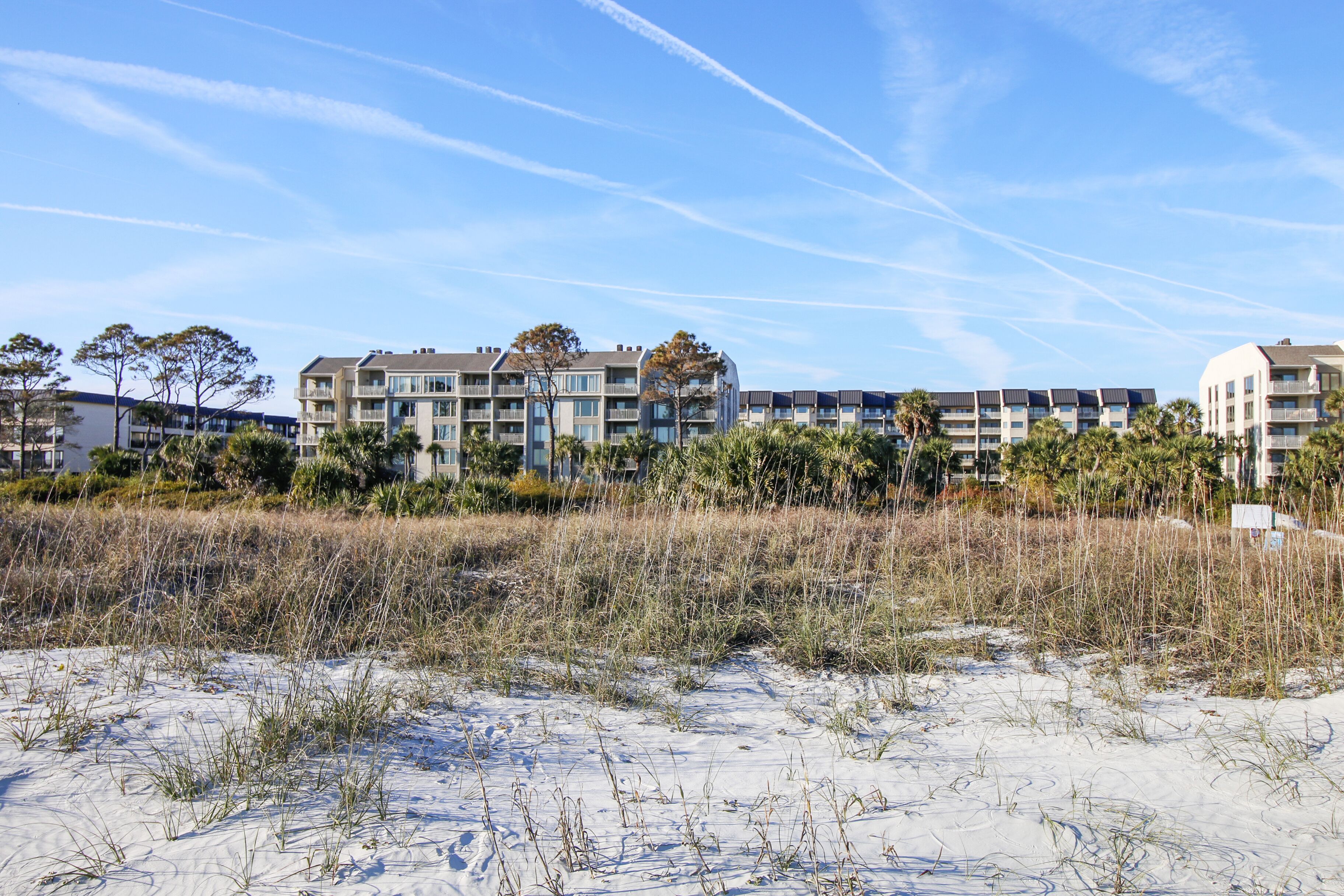 A beachfront hotel with multiple-story buildings, sandy beach in front, and sparse vegetation.