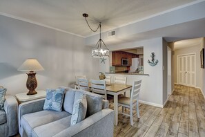 A dining area with a wooden table and chairs, a lamp, and a kitchen in the background.