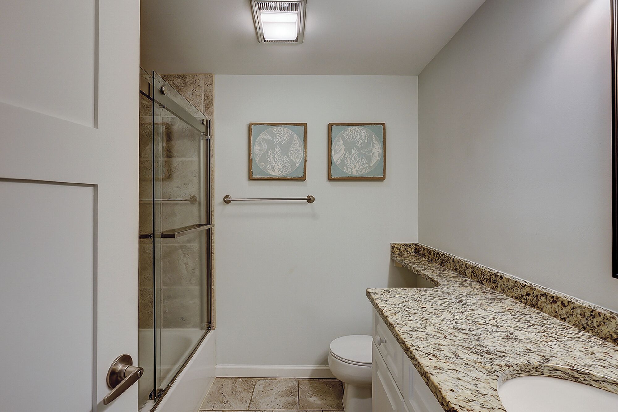 Een badkamer met een douchecabine van glas, een toilet en een aanrechtblad van graniet.