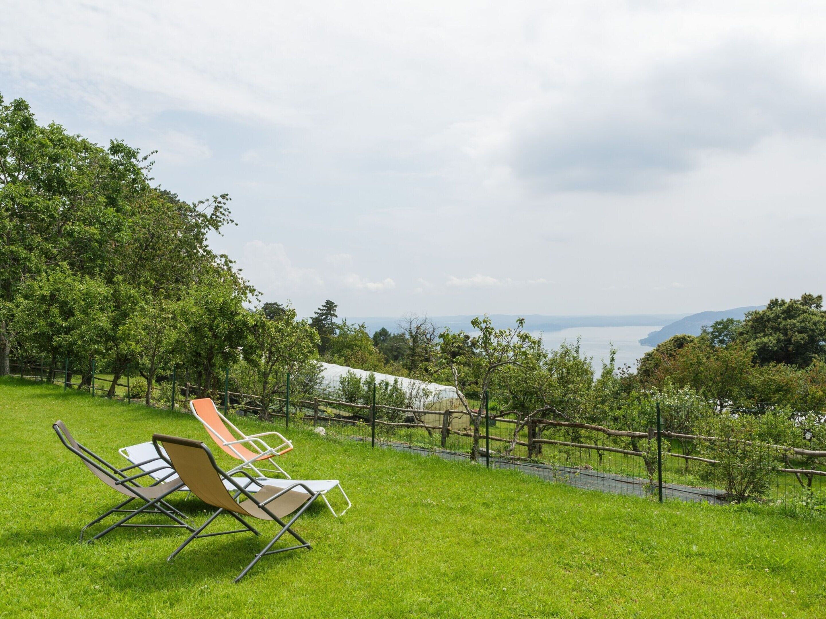 Un espace verdoyant avec deux chaises longues donnant sur un paysage pittoresque, avec un plan d’eau et des collines au loin.