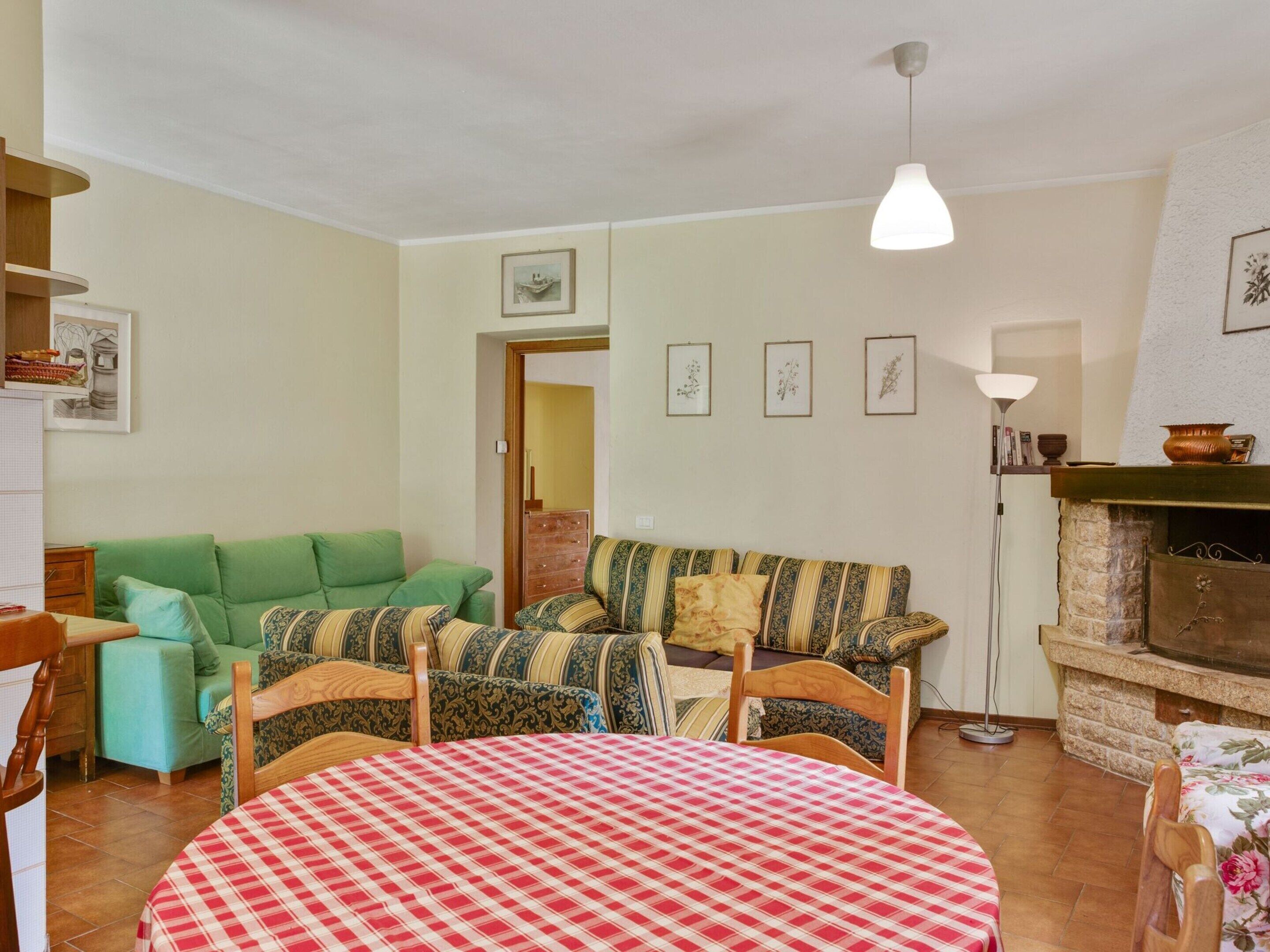 A cozy living room with a green sofa, a patterned sofa, a round table with a checkered tablecloth, and a fireplace.