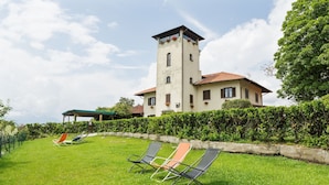 Una casa grande con una torre, un césped y dos sillones.