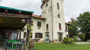 Un edificio con torre, mesas al aire libre y una zona verde.