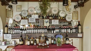 Una bodega con mantel a cuadros rojos, varias botellas de vino y premios enmarcados en la pared.