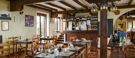 Un comedor rústico con mesas y sillas de madera, una barra con botellas de vino, y vistas al exterior a través de amplias ventanas.