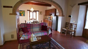 A cozy living room with a sofa, a coffee table, and a rug. There is a kitchen area with cabinets and a refrigerator.