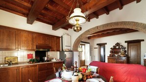A rustic kitchen with wooden cabinets, a dining table set for two, and a red bed in the adjacent room.