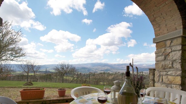 An outdoor dining area with a table set for four, overlooking a scenic landscape with mountains and vineyards.