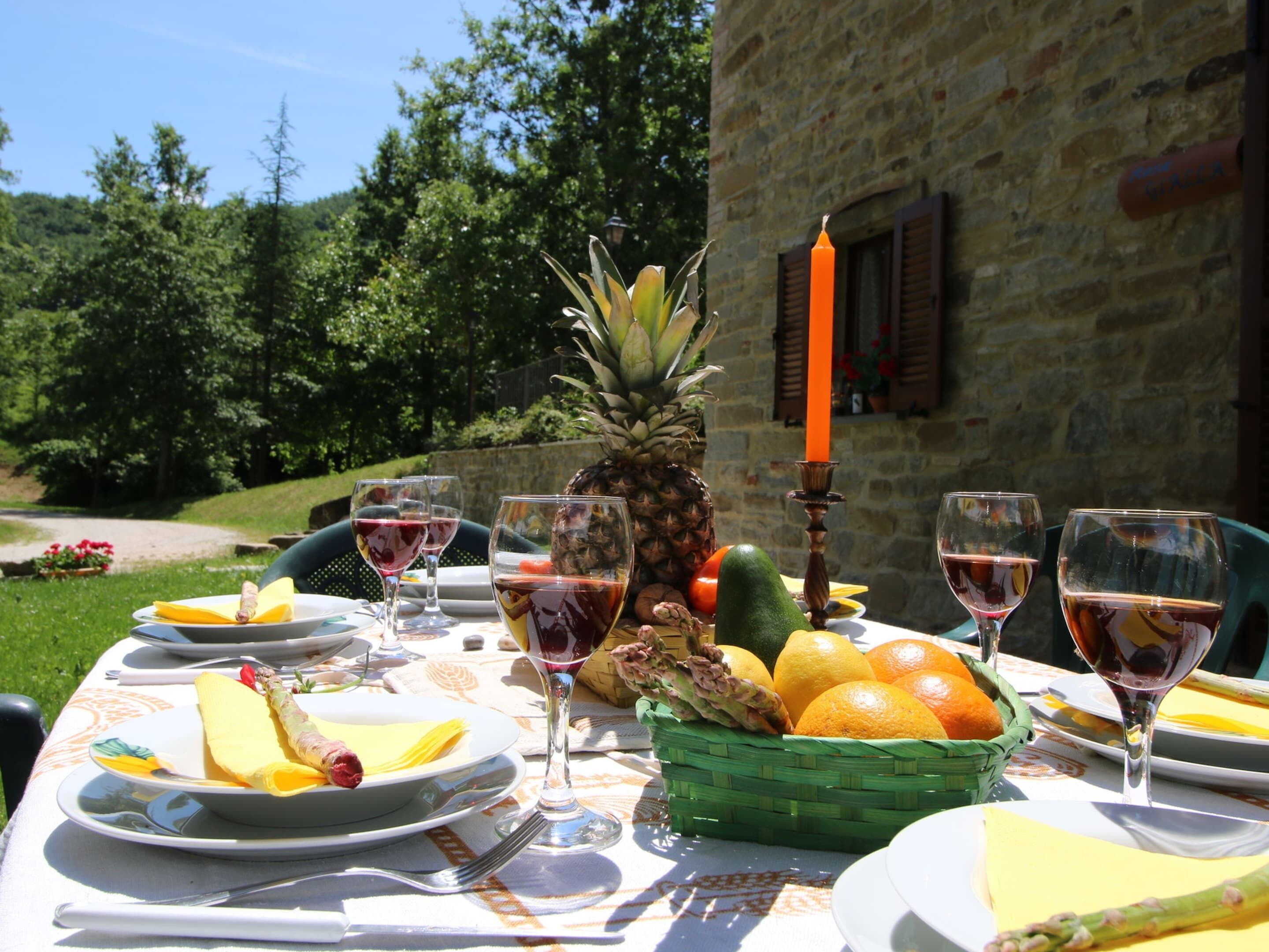 Una mesa de comedor al aire libre con platos, vasos, frutas y una vela.