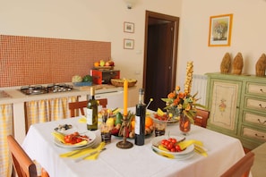 A dining area with a table set for a meal, a kitchen area with a gas stove, and a cabinet with decorative items. - Hill View Retreat w/ Pool (Apecchio)