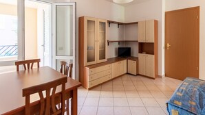 A compact kitchen with wooden cabinets, a dining table with chairs, and a bed with a patterned blanket. - A Sun-drenched Holiday Apartment Near the Sicilian Coastline (Sciacca)