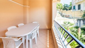 A balcony with a white table and chairs, a tiled floor, and a view of a building and greenery. - A Sun-drenched Holiday Apartment Near the Sicilian Coastline (Sciacca)