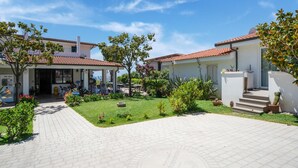 A courtyard with a paved walkway, a covered outdoor seating area, and a building with a tiled roof. - Belvilla by OYO Gattotrilo x 5 (Ricadi)