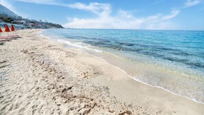 A beach with clear blue water, a sandy shore, and a few umbrellas. - Belvilla by OYO Gattotrilo x 5 (Ricadi)