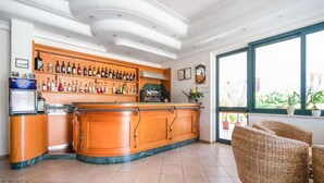 A bar area with a wooden counter, shelves of liquor bottles, and a large window with a view of greenery. - Belvilla by OYO Gattotrilo x 5 (Ricadi)