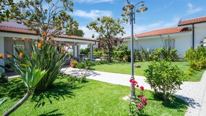 A well-maintained garden with a pathway, a reception area, and a building with a tiled roof. - Belvilla by OYO Gattotrilo x 5 (Ricadi)