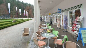 An outdoor cafe area with wicker chairs and tables, a glass display case with postcards, and a signboard with menu options. - Nature & Wellness in Sohl (Bad Elster)