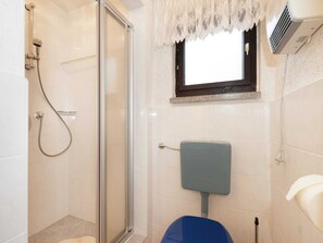 A bathroom with a glass shower enclosure, a toilet, and a window with a lace curtain. - Nature & Wellness in Sohl (Bad Elster)