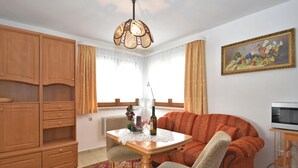 A living room with a wooden cabinet, a dining table with chairs, a sofa, a painting on the wall, and a ceiling light fixture. - Nature & Wellness in Sohl (Bad Elster)