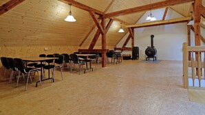 Une pièce spacieuse avec des poutres apparentes, une longue table entourée de chaises et un poêle à bois.