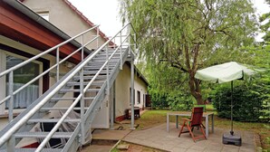Un espace extérieur aménagé, comprenant un escalier en métal menant à une porte, une table avec des chaises et un parasol vert.