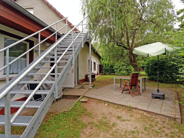 A residential outdoor area with a metal staircase leading to a door, a table with chairs, and a green umbrella. - Forest Getaway in Berlin (Spreehagen)