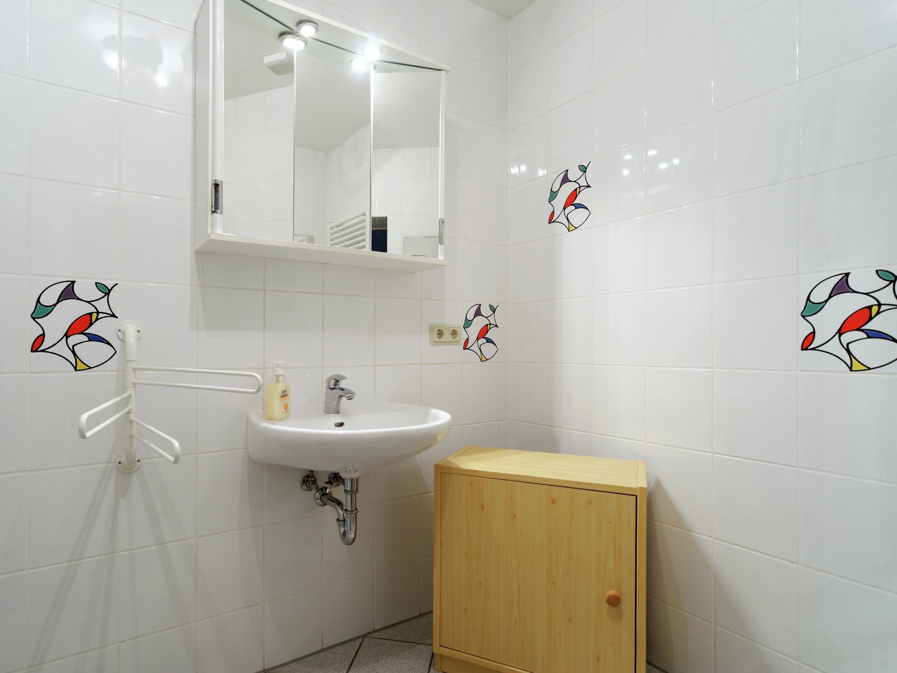 Une salle de bain avec des carreaux blancs, un lavabo, un miroir et un meuble en bois.