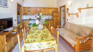 A cozy room with wooden furniture, a dining table with a sunflower tablecloth, a sofa, and a kitchen area with wooden cabinets. - Apartment in Antey-saint-andre Near Ski Lifts (Antey-Saint-Andre)