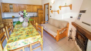 A cozy kitchen with wooden cabinets, a dining table with a sunflower tablecloth, and a sofa. - Apartment in Antey-saint-andre Near Ski Lifts (Antey-Saint-Andre)