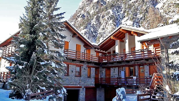 A chalet-style building with a wooden balcony, surrounded by snow-covered trees and mountains. - Apartment in Antey-saint-andre Near Ski Lifts (Antey-Saint-Andre)