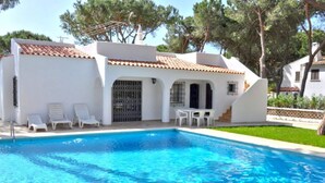 A swimming pool with white lounge chairs and a small table, surrounded by white buildings with tiled roofs. - Lovely and Cozy Golf Villa near Vilamoura Marina (Loulé)
