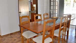 A dining area with a wooden table and chairs, a kitchen in the background, and a view through an open door. - Lovely and Cozy Golf Villa near Vilamoura Marina (Loulé)