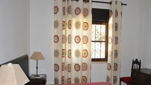 A bedroom with a bed, a nightstand, a lamp, a dresser, and a window with curtains. - Lovely and Cozy Golf Villa near Vilamoura Marina (Loulé)