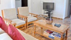 A living room with two wooden chairs, a sofa, a coffee table, a television, and a fan. - Lovely and Cozy Golf Villa near Vilamoura Marina (Loulé)