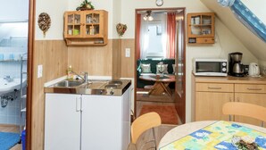 A compact kitchen with a sink, stove, and cabinets, a dining area with a table and chairs, and a view of the living room through a doorway. - Cheerful Apartment near Historic City Center of Haslach (Haslach im Kinzigtal)