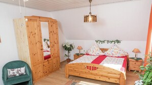 A bedroom with a wooden bed, a green armchair, a wooden wardrobe, and a hanging light fixture. - Cheerful Apartment near Historic City Center of Haslach (Haslach im Kinzigtal)