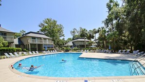 Ein Swimmingpool mit Liegestühlen und Sonnenschirmen, umgeben von Gebäuden und Bäumen.