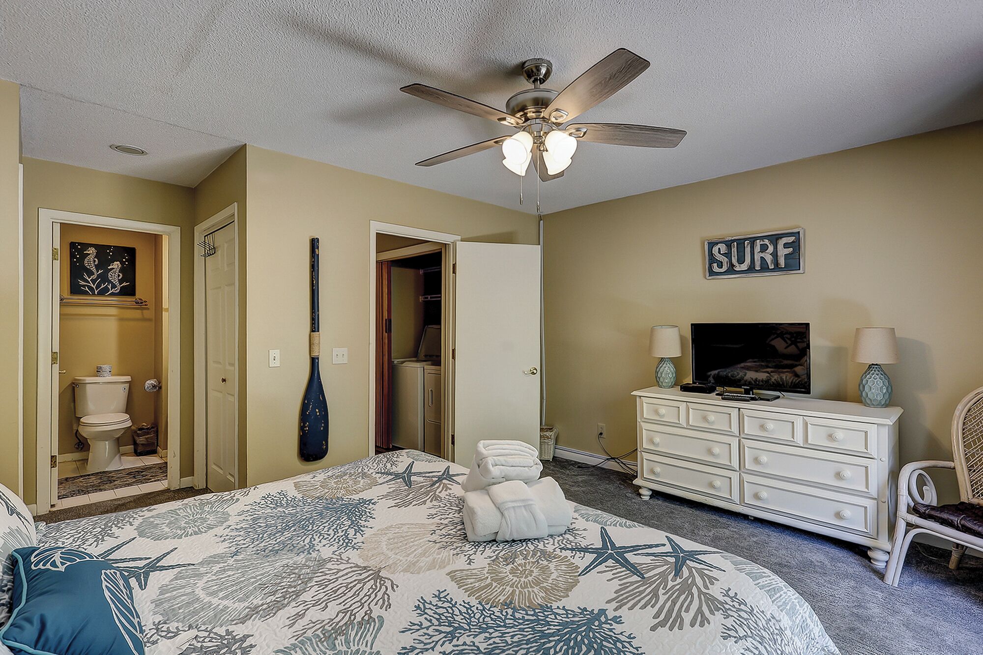 Une chambre avec un lit, un ventilateur de plafond, une télévision, une commode et un panneau sur lequel est écrit « SURF ».